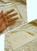 Decorative acrylic wedding card with gold text and tassel, placed on a textured surface.