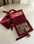 Open red velvet box with chocolates and a card on a white surface