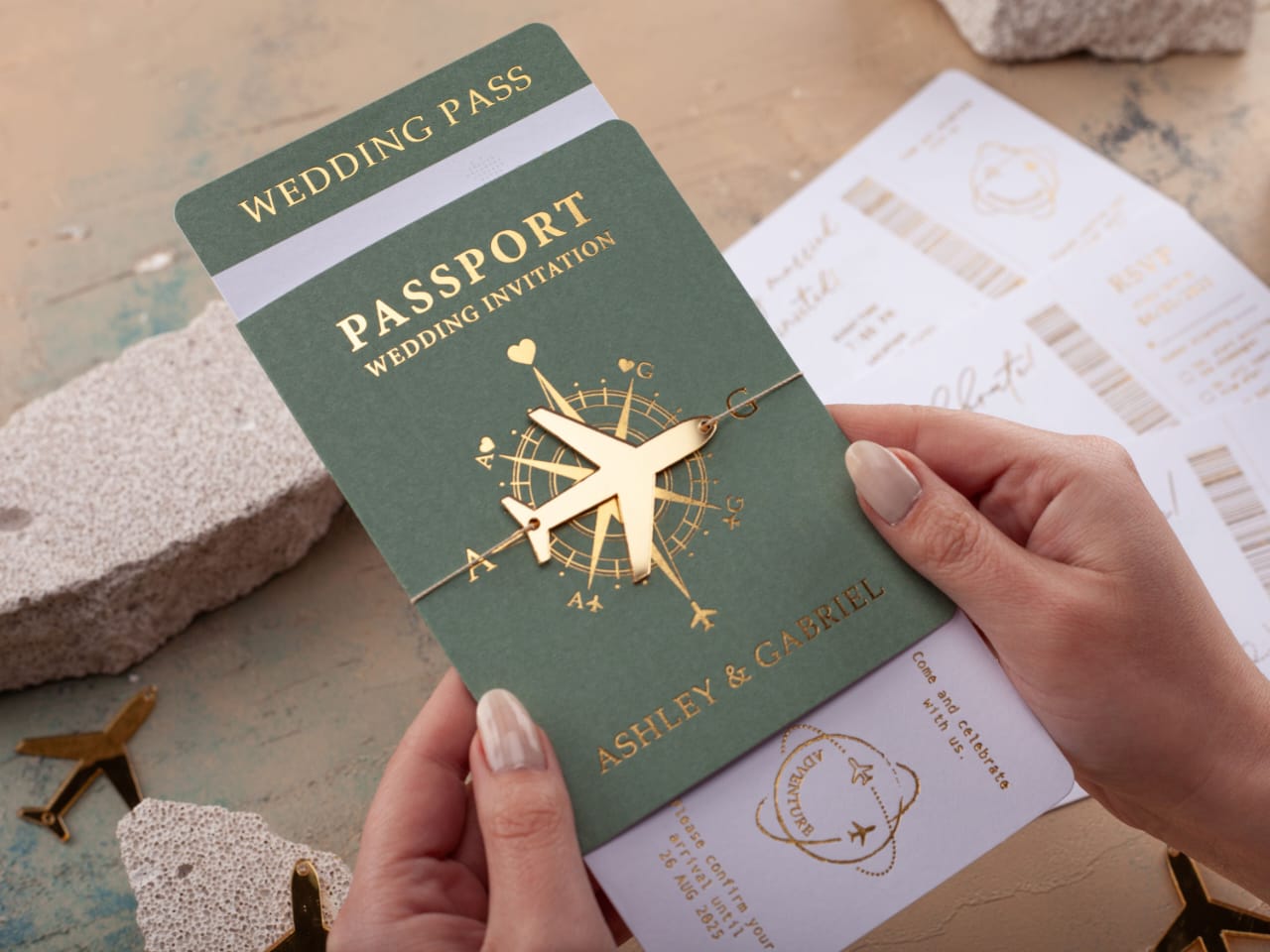 Green passport-style wedding invitation with gold accents held by a hand.