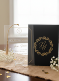 Acrylic card with tassel and black card with gold design on a wooden surface.