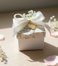 Small bid box with a white ribbon and decorative tag on a wooden surface with baby's breath flowers.