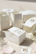 White bid boxes with gold text on a light surface with baby's breath flowers.