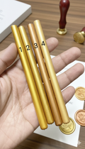 Gold glue gun wax rod with numbers on a wooden surface