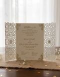 pakistani wedding invitation with laser cut-out design on a wooden surface with flowers.