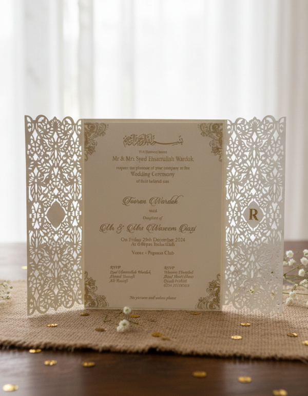 pakistani wedding invitation with laser cut-out design on a wooden surface with flowers.