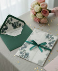 Invitation cards with green envelopes and ribbons on a table with flowers.