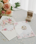 Floral invitation card with envelope and ring box on a table with flowers in the background
