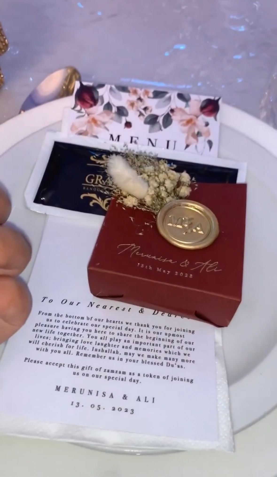 A customized favor box with a floral design, a red seal stamp, and a personalized message displayed on a white plate.