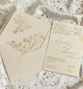 Beige wedding invitation with floral design on a white fabric background with gold sequins