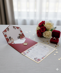 Floral wedding invitation set with a ring box and bouquet on a table.