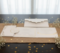 This image displays an elegant designer wedding invitation set, featuring a sophisticated white and gold color scheme. The collection includes various cards with ornate gold foil printing, enhancing the luxurious feel.


